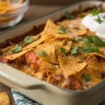 A freshly baked Mexican Chicken Casserole with Doritos in a casserole dish, topped with melted cheese and crispy, golden Doritos, garnished with fresh cilantro.